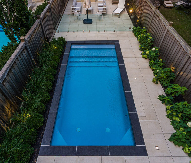 Aerial view of a landscaped backyard featuring a pool, lawn, and surrounding greenery.