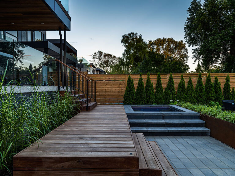 Backyard view with a modern pool, stylish patio, and lush greenery.