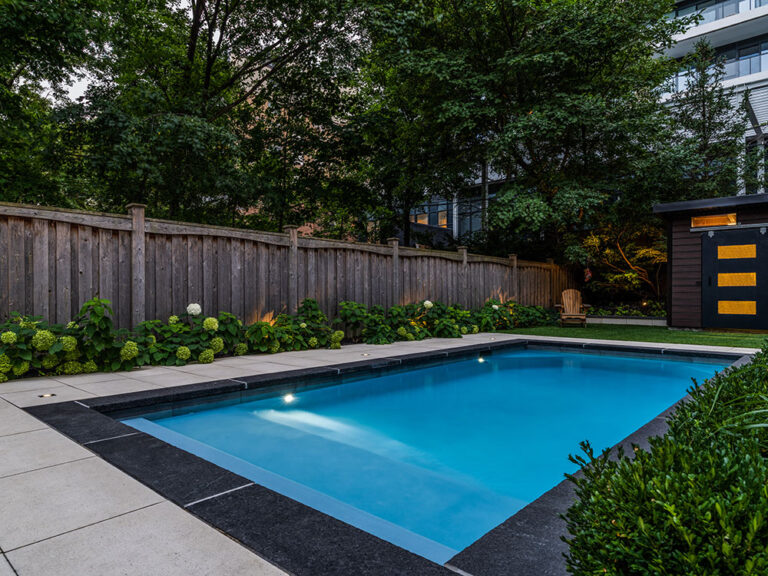 Close-up of a modern backyard pool area with stone patio and lounge chairs.