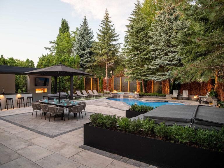 Spacious backyard with stone patio, modern outdoor furniture, and greenery.