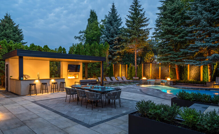 Elegant backyard pool design with surrounding stone patio and lush green landscaping.