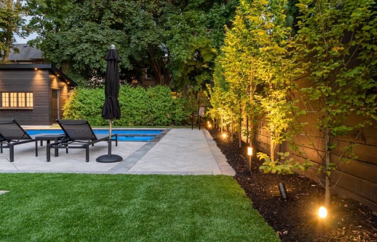 Elegant backyard pool area featuring a wooden deck, lounge chairs, and greenery.